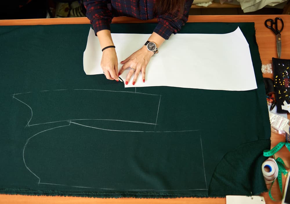 Pattern maker marking an inner-short pattern on dark green fabric before activewear sampling