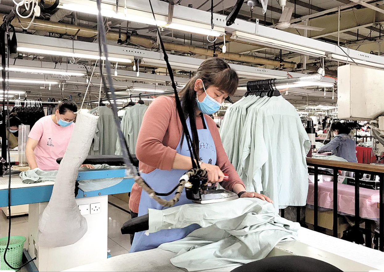 Garment worker pressing finished clothing during an order preparation stage