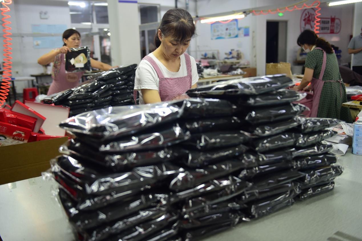 User-provided editorial factory-packing reference showing unbranded black garments being prepared in protective bags